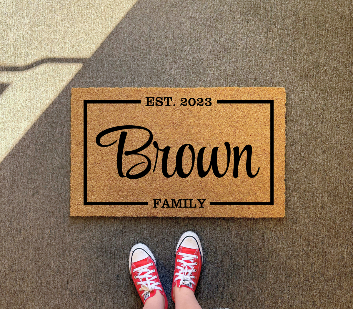 Family name special date doormat with Brown, EST. 2023 and FAMILY inside a frame, on dark gray pavement