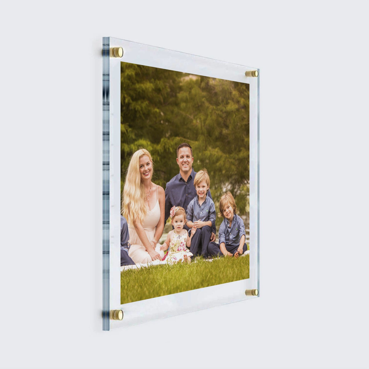 Angled view of a family photograph inside a clear floating acrylic frame with gold mounts.