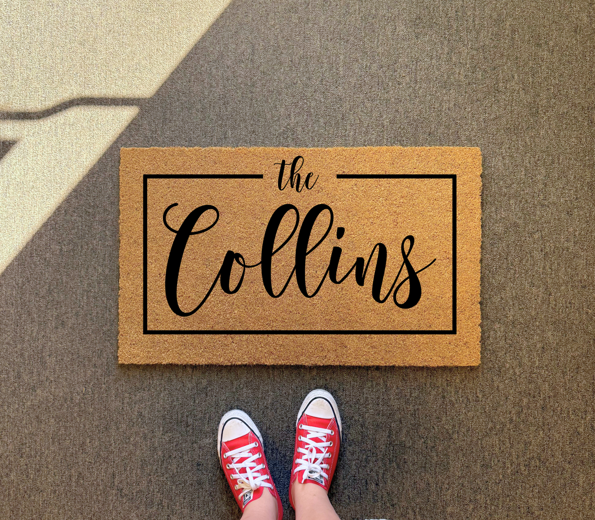 Framed family name doormat with sample name The Collins on dark gray pavement, red sneakers at its edge