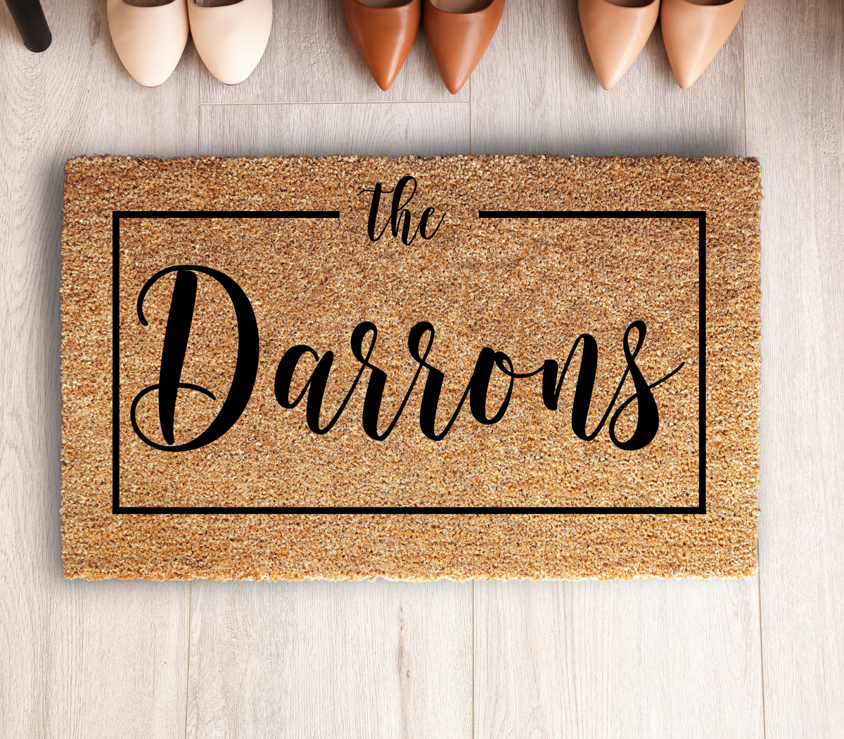 Framed family name doormat with sample name The Darrons on a wood floor above a row of pointed-toe shoes