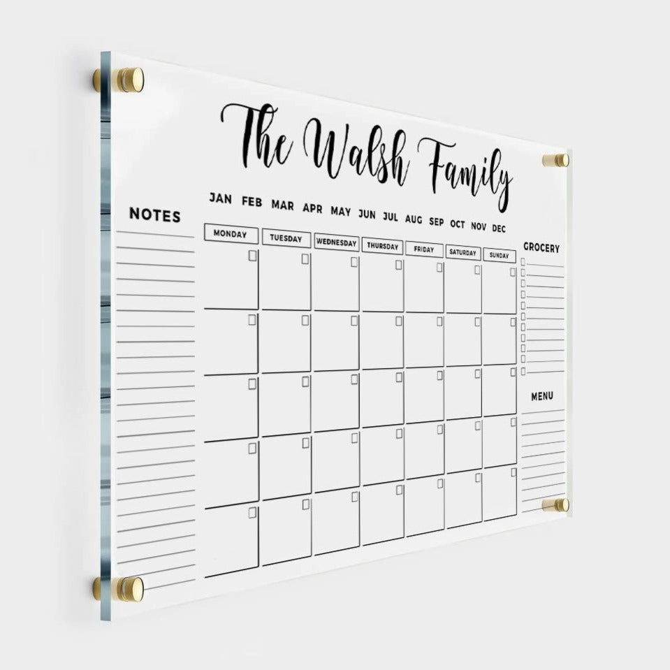 Clear acrylic monthly family calendar with a custom family name heading, three side sections for lists and gold wall mounts.