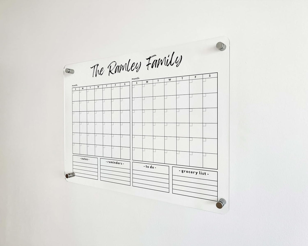 Angled detail of a clear acrylic calendar with two adjacent monthly grids and four lined list sections below.