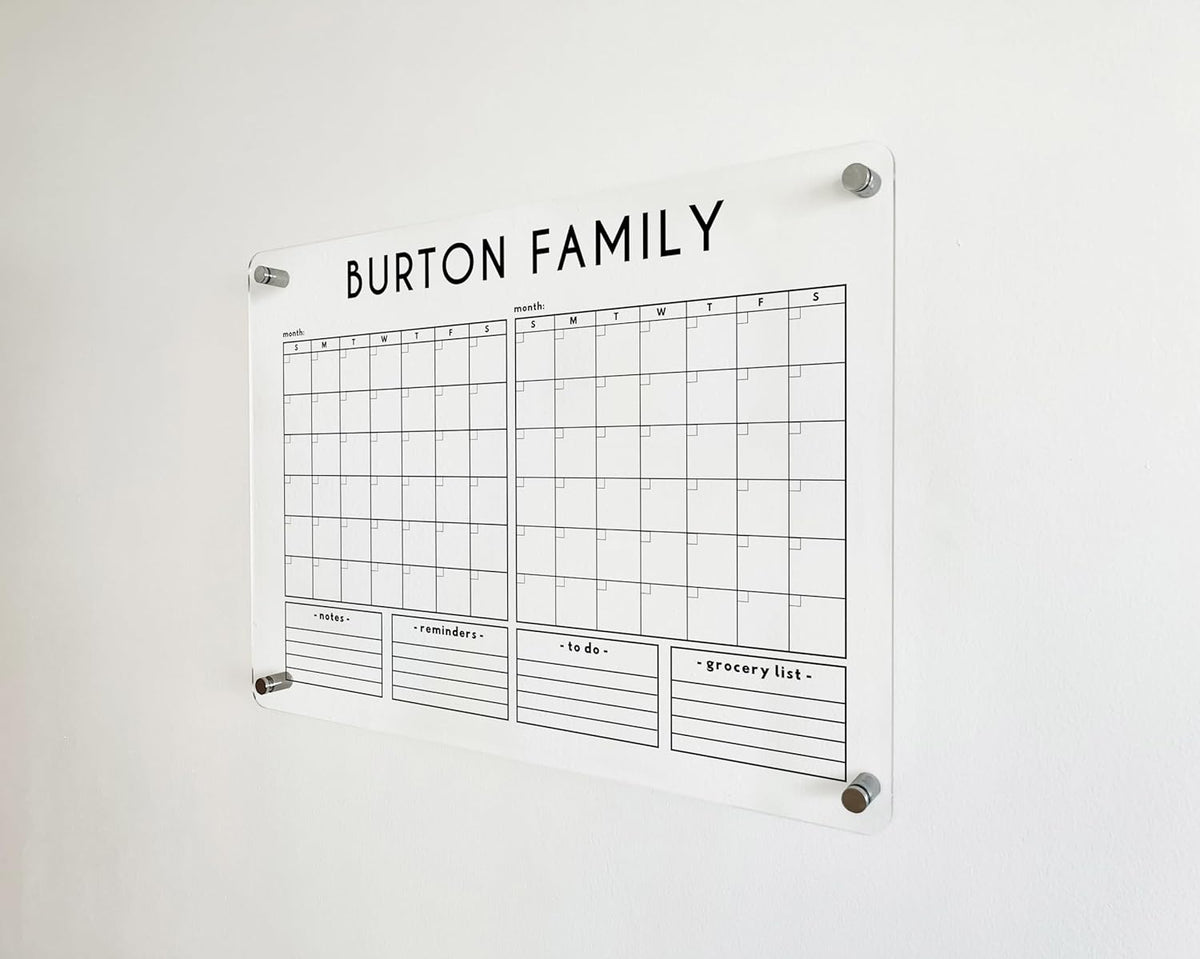 Angled detail of a clear acrylic family calendar with two monthly grids and four custom list headings.