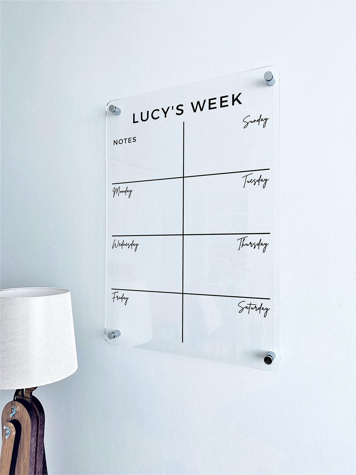 Vertical clear acrylic weekly planner mounted beside a lamp, with a custom heading, seven day spaces and a Notes area.