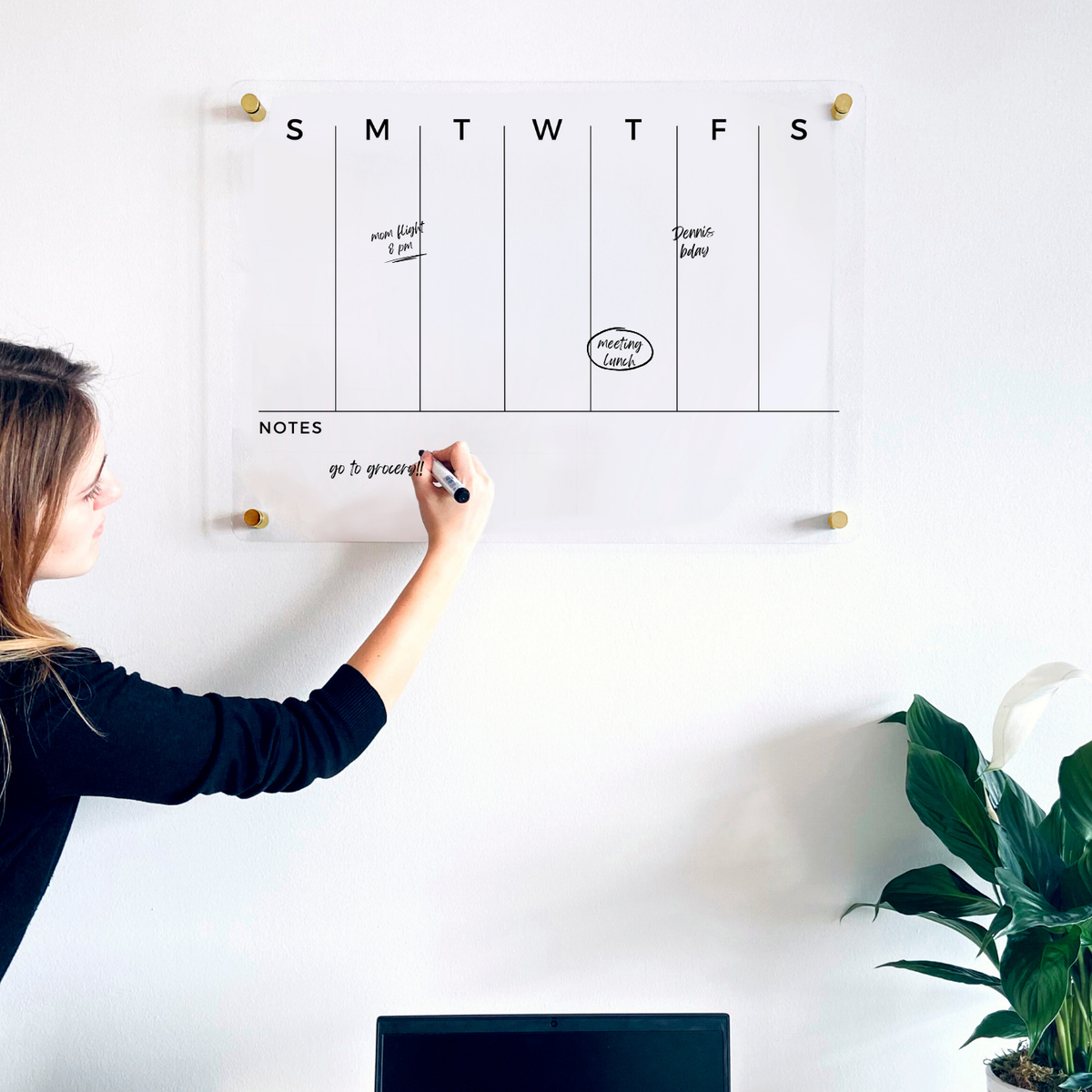 A person writing on a clear acrylic weekly planner with seven day columns and a lower Notes area.