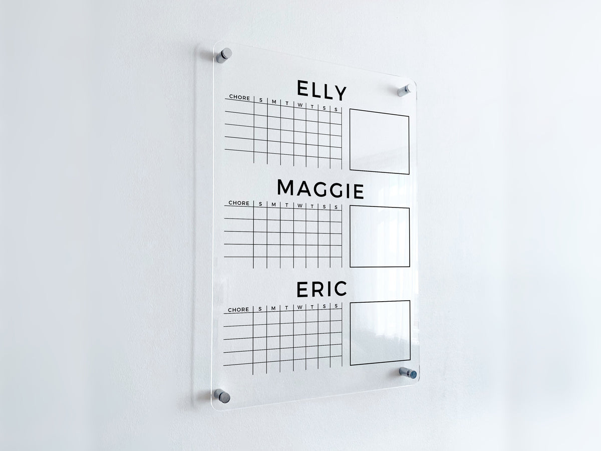 Angled view of a clear acrylic chore chart with three custom name headings, weekly task grids and blank note boxes, mounted with silver hardware.