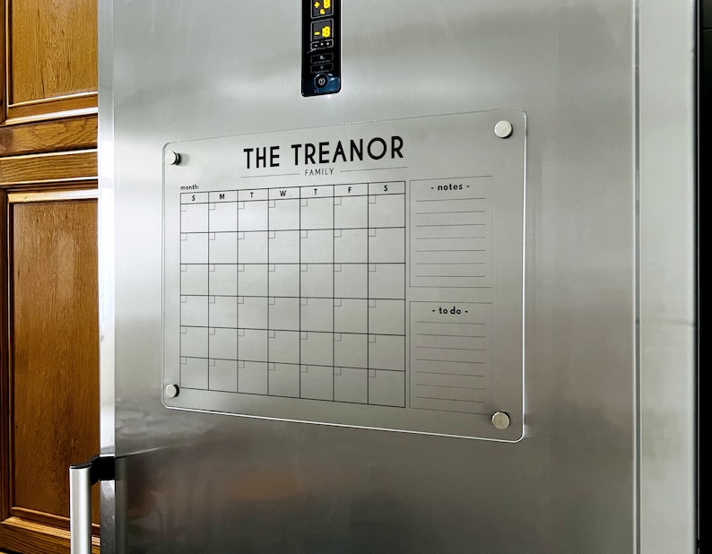 Magnetic acrylic fridge board with a monthly grid, a family subtitle, and notes and to-do lists on the right.