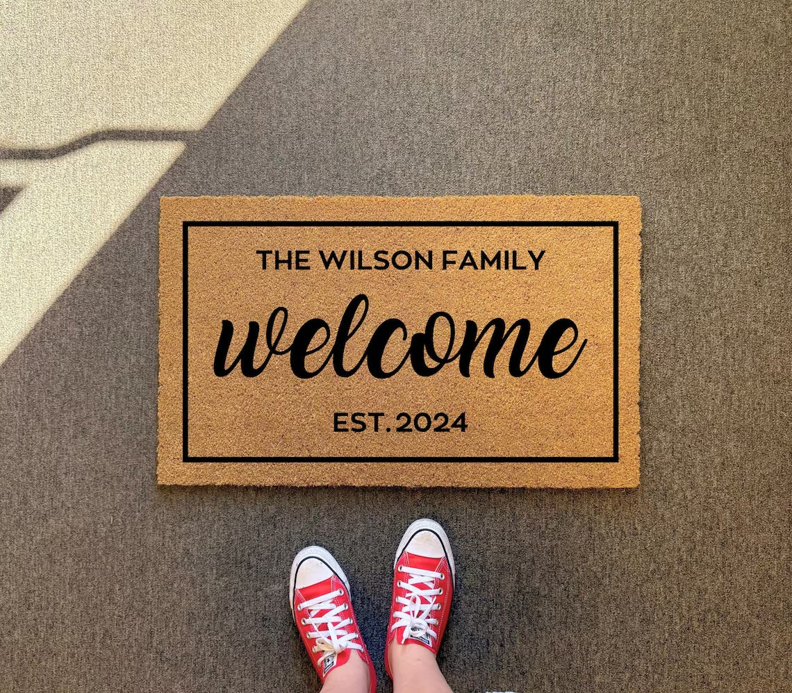 Welcome Customized doormat with sample text THE WILSON FAMILY, EST. 2024, on dark gray pavement, red sneakers