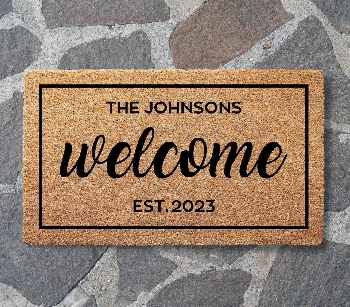 Welcome Customized doormat with sample text THE JOHNSONS, EST. 2023, laid on gray flagstone paving