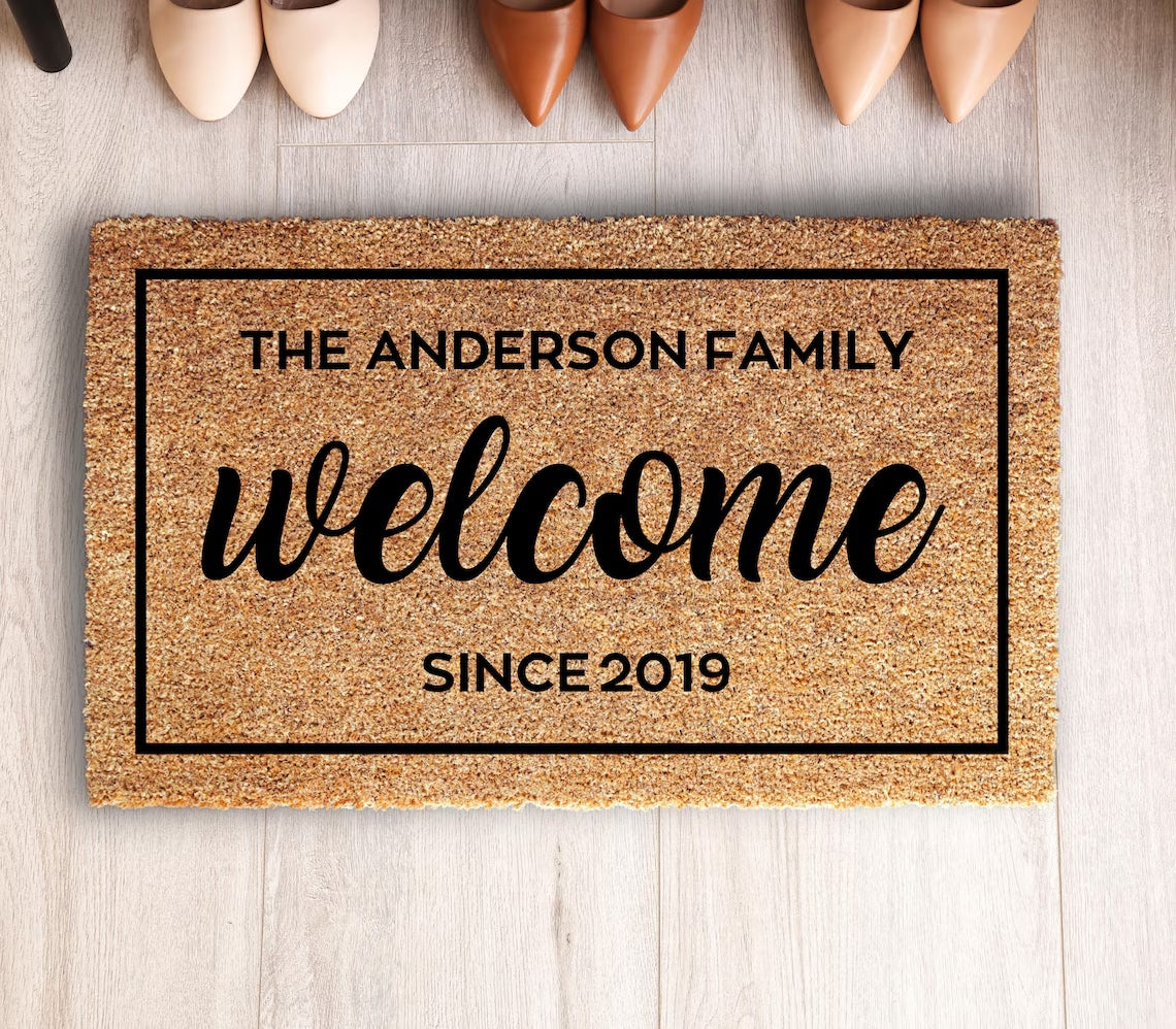 Welcome Customized doormat with sample text THE ANDERSON FAMILY, SINCE 2019, on a wood floor above shoes